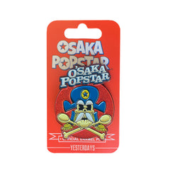 Enamel pin of Osaka Popstar Crunchy featuring cartoon skull with blue hat and crossbones